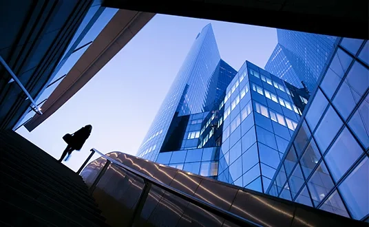 Person steigt eine Treppe hinauf; moderne Glas-Hochhäuser im Finanzviertel
