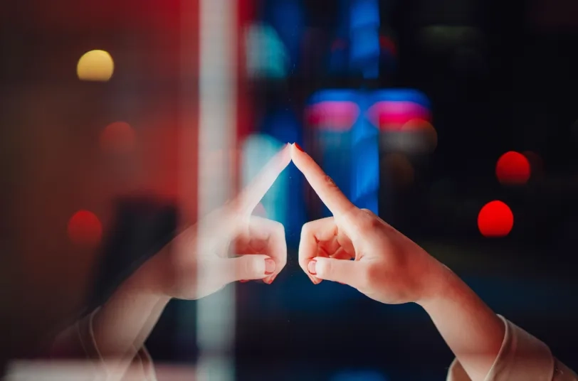 Hand, die eine Glasfläche berührt, mit Spiegelung und Lichtpunkten im Hintergrund
